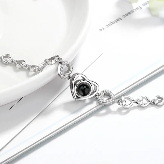 Silver heart-shaped necklace with a central black stone, adorned with smaller heart links and sparkling accents.
