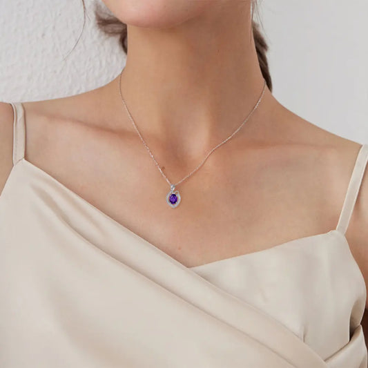 Elegant woman wearing a delicate silver necklace with a purple gem pendant, showcasing her collarbone in a soft beige dress.