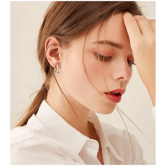 A close-up of a woman wearing stylish silver hoop earrings with a decorative gemstone, styled with soft, wavy hair.