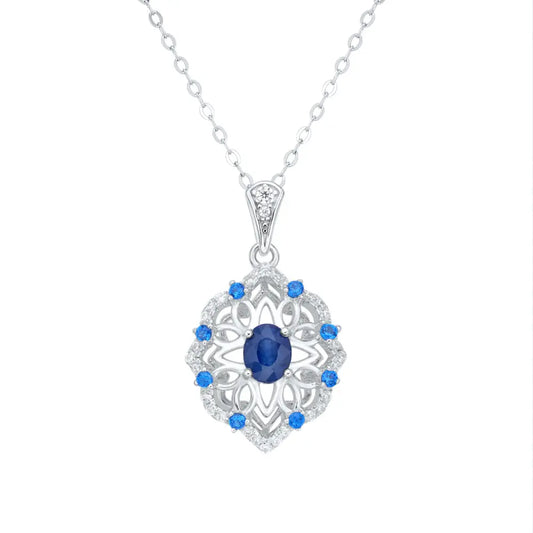 Silver pendant necklace featuring a central blue sapphire surrounded by smaller blue stones, set on a delicate chain against a white background.
