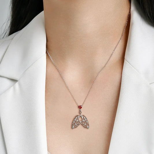 Close-up of a woman wearing a silver necklace with a wing-shaped pendant, featuring a red gemstone and intricate detailing.