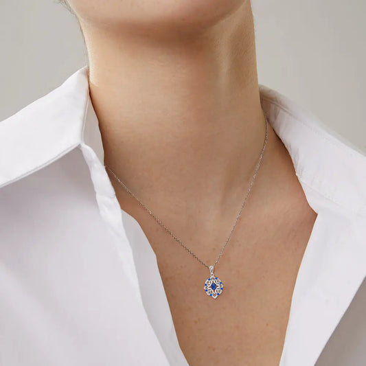 Close-up of a woman's neck wearing a silver chain necklace with a blue floral pendant, styled with a white collared shirt.