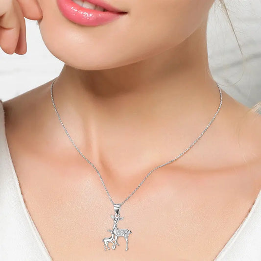 A close-up of a woman's neck featuring a silver necklace with a delicate deer and fawn pendant, complementing her smile.