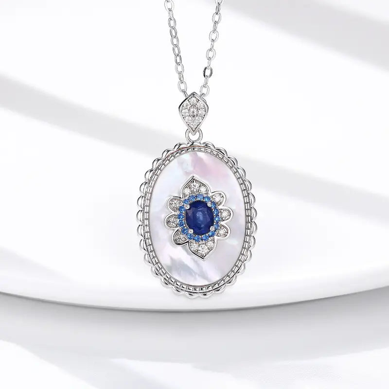 Elegant silver pendant featuring a central blue gemstone surrounded by sparkling diamonds, set against a mother-of-pearl backdrop.
