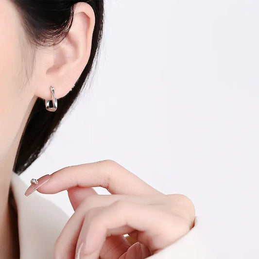 Stylish silver hoop earrings with a twisted design, displayed on a textured stone surface with a dark background.